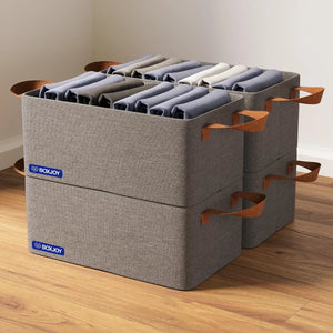 Four grey BOXJOY stackable fabric storage boxes filled with folded clothes on a wooden floor.